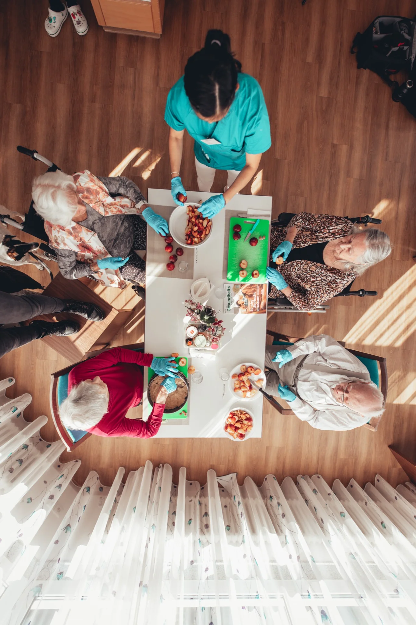 Gruppenaktivität in der Sozialstation Karlsruhe: Senioren sitzen um einen Tisch und bereiten gemeinsam mit Pflegepersonal Obst vor. Projektbegleitung und Fotografie von syd.media für die Stadtmission.