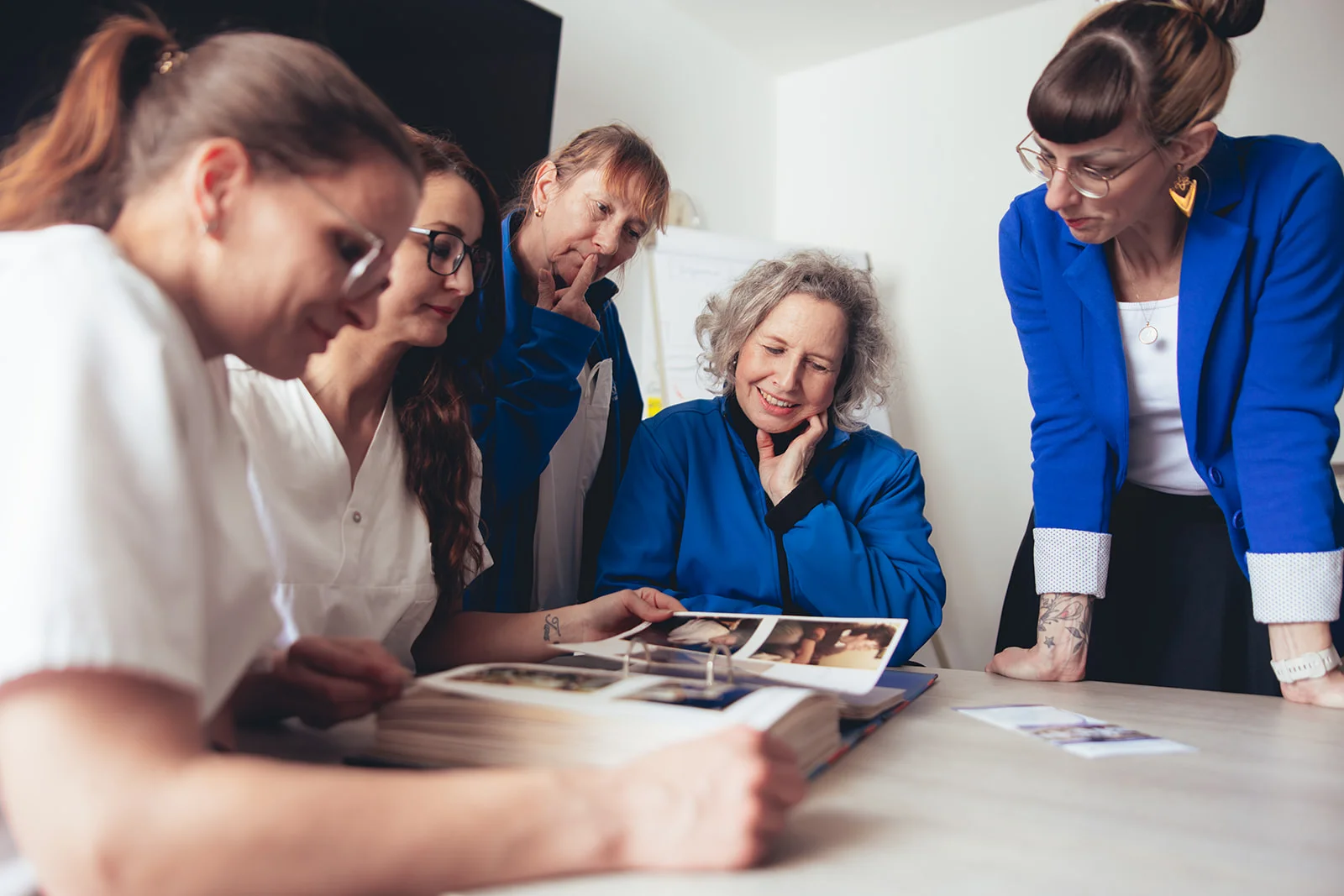 Ein Team von Pflegekräften und Betreuern der Sozialstation Karlsruhe betrachtet gemeinsam ein Fotoalbum, das Erinnerungen und Geschichten festhält. Diese Szene unterstreicht die Bedeutung von persönlicher Pflege, Empathie und gemeinsamer Geschichte. Passend für Inhalte im Bereich Fotografie, Projektbegleitung und Storytelling zur Darstellung der einfühlsamen Betreuung durch die Sozialstation.